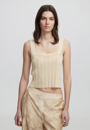 Top corto de canalé crema con tirantes anchos, escote cuadrado y dobladillo sin acabar. Combinado con pantalones anchoss de pierna ancha en un beige claro y con estampado.