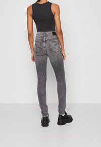 Jeans skinny grises con cintura alta, con textura de denim y bolsillos traseros, combinados con botas negras de suela gruesa.