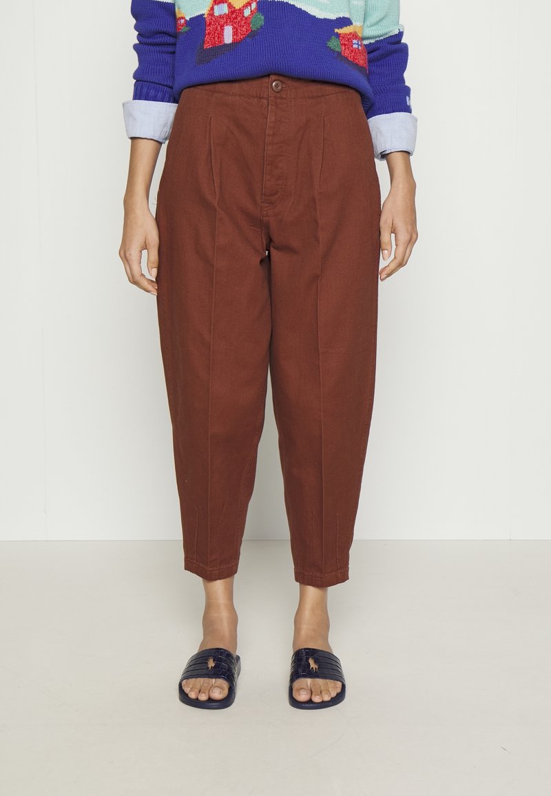 Bruna, höga byxor med framtill vikningar, avsmalnande anklar och knappstängning. Matchad med marinblåa sandaletter med texturerade remmar.