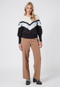 Black, cream, and light blue knit sweater with a chevron design; paired with tan wide-leg pants and shiny black platform shoes.