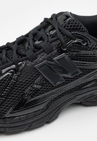 Vue en gros plan d'une chaussure de sport noire avec tissu en mesh, semelle texturée et logo audacieux "N" sur le côté.