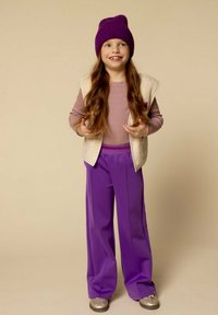Kinderoutfit bestaande uit een crèmekleurige gilet, paarse beanie, gestreept langslijf top en brede paarse broek, aangevuld met zilveren schoenen.