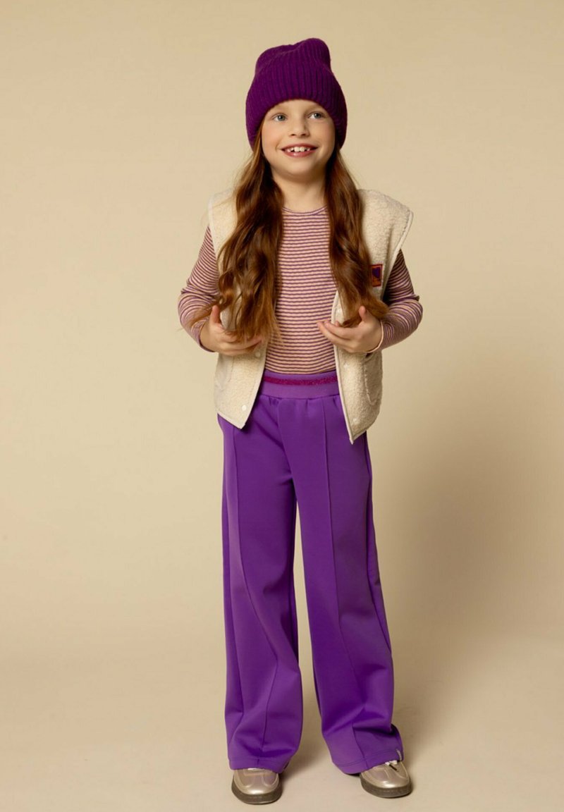 Kinderoutfit bestaande uit een crèmekleurige gilet, paarse beanie, gestreept langslijf top en brede paarse broek, aangevuld met zilveren schoenen.