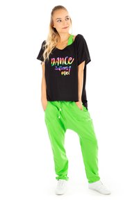 Crna oversized majica sa šarenim natpisom "DANCE defines me!", uparena sa zelenim treniranim hlačama. Ima slobodan kroj i ležeran dizajn.