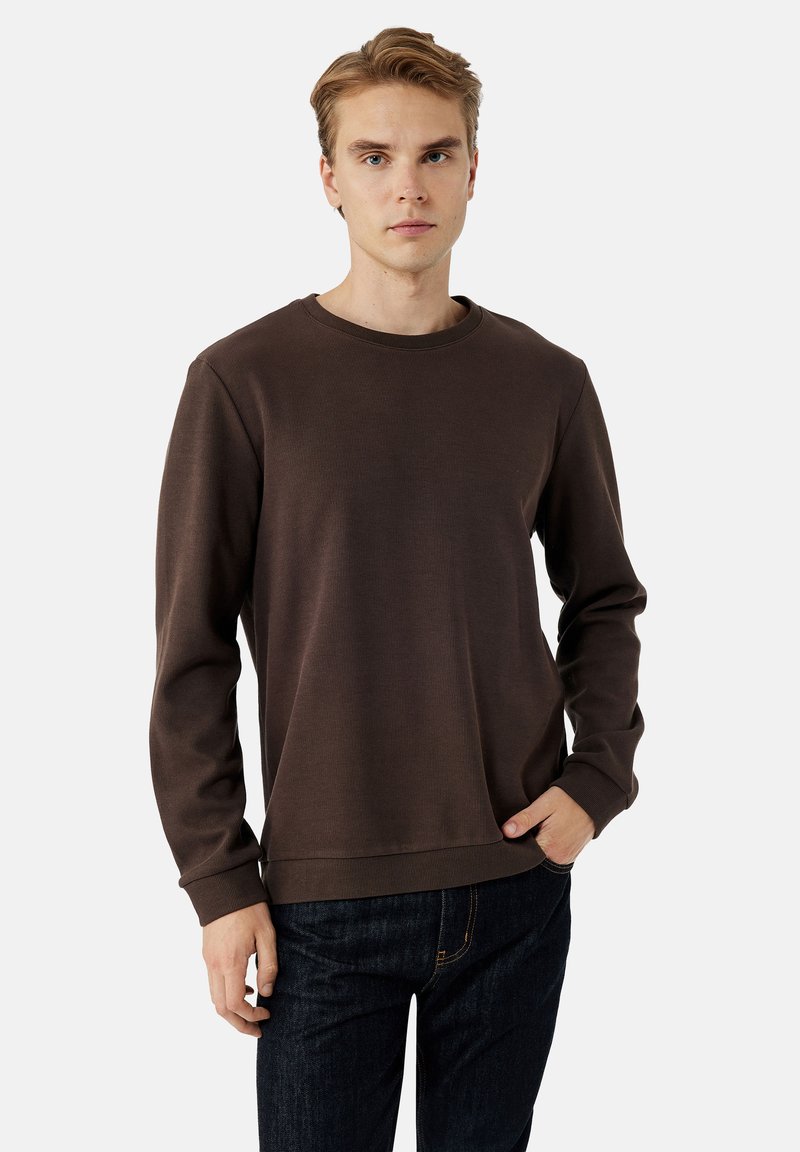 Bruine sweatshirt met lange mouwen, een geribbelde textuur, een ronde halslijn en een ontspannen pasvorm. Gecombineerd met donkerdenim jeans. Minimalistisch ontwerp.