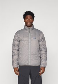 Šedý prošívaný kabát s stojáčkem, zipovým zapínáním vpředu a malým logem na levém prsu. Elegantní, prošívaný design s bočními kapsami.