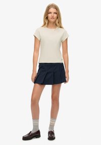 Camiseta de manga corta beige combinada con una falda plisada a rayas marino. Medias a rayas grises y mocasines burdeos completan el conjunto.