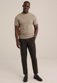 Kratký pletený svetr v béžové barvě s kulatým výstřihem, spárovaný s těsnými tmavě hnědými kalhotami a černými mokasíny, na neutrálním pozadí.