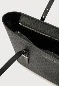 Mala preta com exterior em tecido texturizado, fecho de correr e alça de couro. No interior apresenta um forro preto liso.