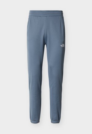 Pantalones de forro polar azul con corte cónico, cintura elástica y puños elásticos, con un pequeño logo blanco de The North Face en el muslo derecho.