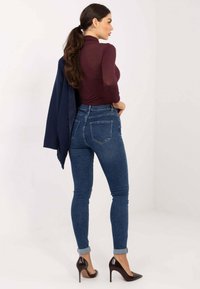 Hoch taillierte blaue Jeans aus Denim mit figurbetonter Silhouette, umgeschlagenen Säumen und zwei Gesäßtaschen, kombiniert mit einem burgunderroten Langarmshirt.