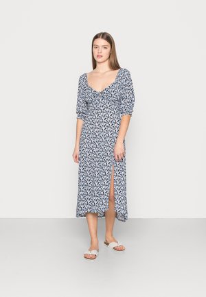 Vestido com padrão floral em azul e branco, apresentando decote arredondado, mangas bufantes, uma fenda frontal e tecido leve.