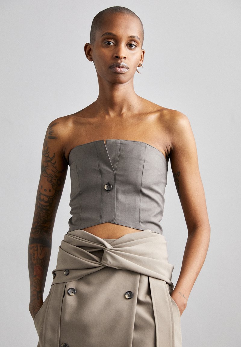 Gray strapless top with structured design, front button detail, and textured fabric; paired with a beige high-waisted, knotted skirt.