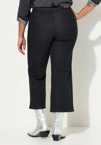 Pantaloni neri in denim a gamba dritta e a vita corta, con due tasche posteriori. Abbinati a stivali alla caviglia in argento lucido.