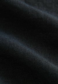 Čierna tkanina s textúrovaným povrchom, prejavujúca jemný úplet. Materiál sa zdá byť mäkký s jemným leskom na svetle.