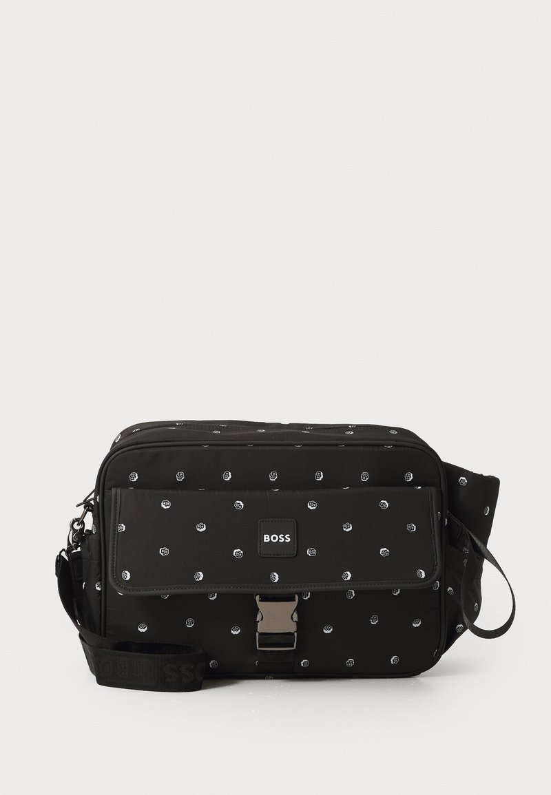 Juodas messenger krepšys, pagamintas iš nailono su baltu taškų raštu, turi priekinę uždengimą, sidabro spalvos metalinius elementus ir petį diržą su logotipo detalėmis.