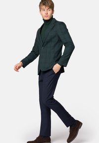 Zielona marynarka w kratę o dopasowanym kroju, noszona na ciemnym golfie. Połączona z granatowymi spodniami i brązowymi zamszowymi butami.