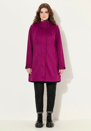 Fuchsia hængekappe med lige snit, forlommer og justerbar krave. Bæret sammen med mørke jeans og sorte snørebåndsstøvler.