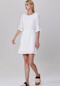 Robe blanche courte avec des manches bouffantes, ornée de dentelle et en tissu texturé. Le design comprend une taille ajustée et une jupe fluide.