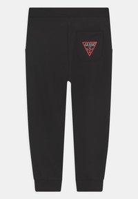 Schwarze Sweatpants aus weichem Stoff mit tapered Beinen. Mit einer roten, dreieckigen Aufsetztasche mit Logo-Detail auf der Rückseite.