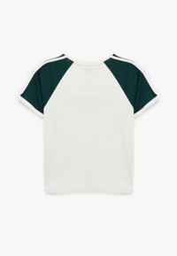 Valkoinen lyhythihainen t-paita tummanvihreillä raglan-hihalla ja valkoisilla raidallisilla yksityiskohdilla. Valmistettu teksturoidusta kankaasta, jossa on pyöreä kaula-aukko.