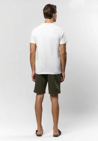 Bijela majica kratkih rukava od pamuka, u paru s maslinasto zelenim šortsem. Šorts ima glatku teksturu i opušteni kroj.
