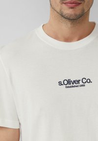 Witte katoenen T-shirt met ronde hals en korte mouwen, met het marineblauwe tekstlogo "s. Oliver Co. Established 1969" op de borst.