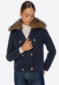 Marineblazer mit doppelter Brustreihe, Kragen aus Kunstfell, großen goldenen Knöpfen und strukturiertem Stoff. Mit seitlichen Taschen und verkürztem Schnitt.