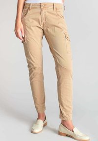 Pantalones cargo beige con un ajuste entallado, que presentan bolsillos frontales y laterales, cierre de botón y una tela ligera y texturizada.