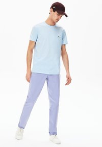 Camiseta de algodón azul claro con cuello redondo, combinada con pantalones ajustados lavanda. El modelo lleva una gorra de béisbol burdeos y zapatillas blancas.