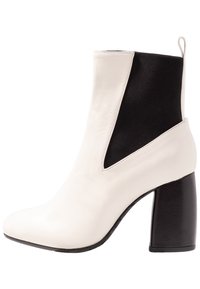 Bílé kožené kotníkové boty s černým elastickým panelem, špičatou špičkou a robustním černým podpatkem. Vyznačují se čistými liniemi a minimalistickým designem.