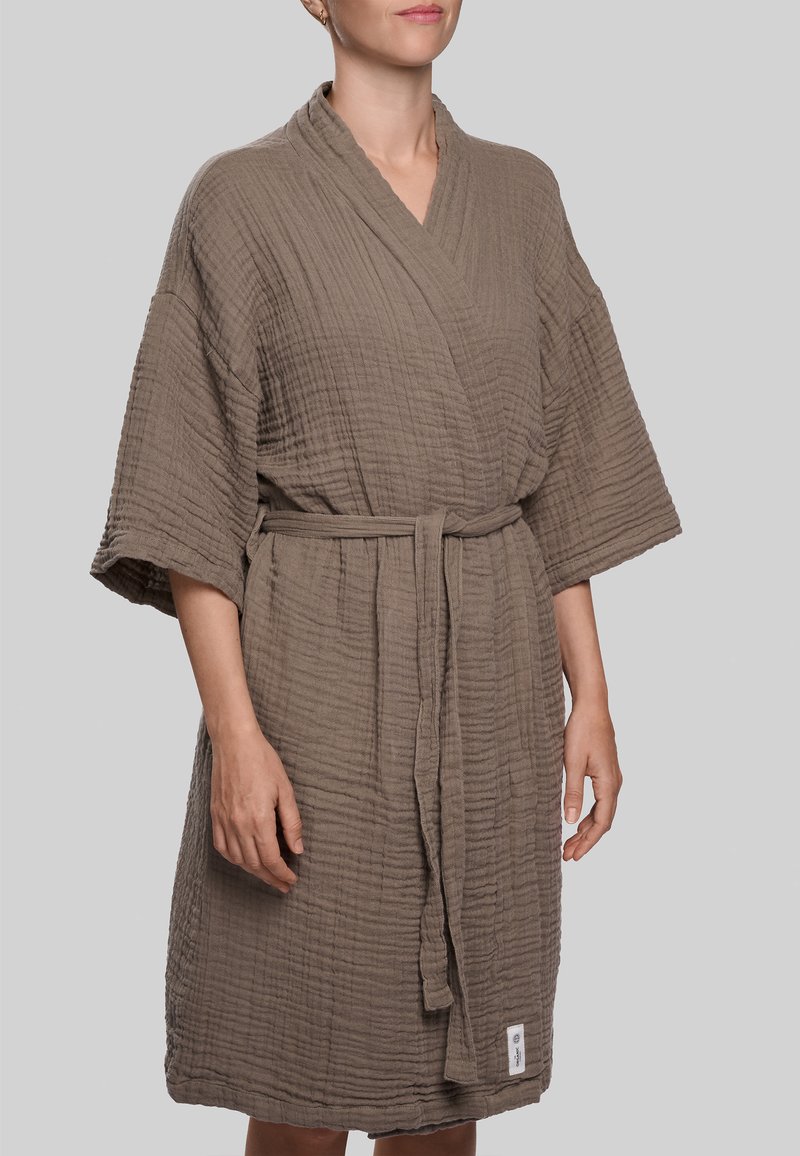 Rudas tekstūruotas chalatas su apvyniojamu dizainu, plačiomis rankovėmis ir diržu. Yra etikėtė prie krašto ir raukšlėtos audinio išvaizdos.