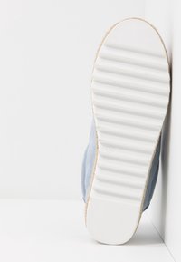 Chaussure bleu clair avec une tige en tissu texturé et une semelle en caoutchouc blanche présentant des rainures horizontales et un bout arrondi. Taille marquée comme 37.