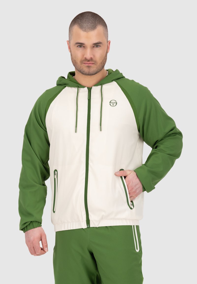 Giacca verde e crema con zip e cappuccio, maniche raglan a contrasto e due tasche con zip. Materiale sintetico con texture liscia.