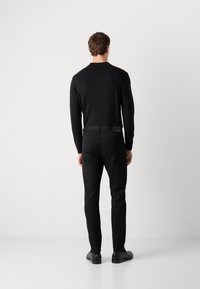 Svart langermet skjorte med rund hals, paret med svarte slim-fit bukser. Har et merke på linningen og skinnteksturerte detaljer.