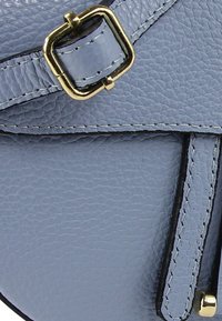 Lichtblauwe handtas van textuurleer met gouden accenten. Heeft een vierkante gesp en contrasterend stiksel langs de randen.
