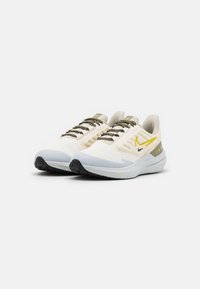Zapatillas de running ligeras en blanco y gris, con una parte superior texturizada, cordones verdes y una suela de goma negra con acentos amarillos.