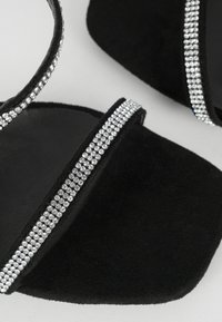 Sandali in suede nero con una larga fascia decorata con una fila di strass trasparenti, design a punta quadrata e suola piatta.