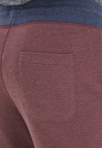 Bordo trenirke s plavim pojasom, s jednim stražnjim džepom i mekim materijalom. Jednostavan dizajn s minimalnim šavnim detaljima.