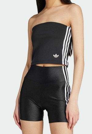 Nainen pukeutuneena mustaan olkaimettomaan lyhytpaitaan ja korkeavyötäröisiin shortseihin, molemmissa valkoiset sivuraidat ja Adidas-logo paidassa.