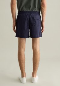 Costumi da bagno blu navy con fascia elastica in vita, tasca posteriore singola e tessuto leggero. Design minimalista con una texture liscia.