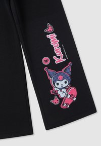 Czarne dresy mają kolorową grafikę postaci na deskorolce z różowymi akcentami oraz napisem "Kuromi" obok zabawnych ikon.