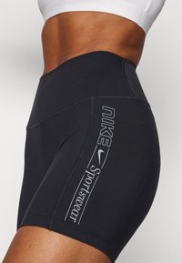 Pantaloni sportivi neri Nike con vita elasticizzata, dotati di cuciture piatte e logo laterale grigio. Il tessuto sembra liscio ed elasticizzato.