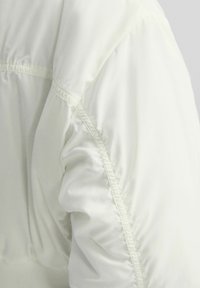 Nadmuchana, biała rękaw kurtki z elastycznymi szwami, gładka faktura i subtelny połysk. Posiada marszczone tkaniny dla luźniejszego dopasowania przy nadgarstku.