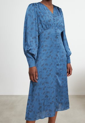 Femme portant une robe midi bleue à motif cachemire, manches longues bouffantes, poignets smockés et corsage à col en V boutonné.
