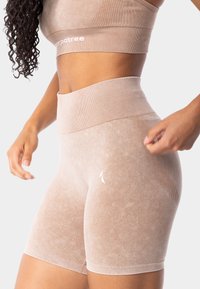 Béžové šortky s vysokým pasem, žebrovaným pasem, jemným leskem, bezšvovým designem a malým bílým logem na boku. Měkká textura.