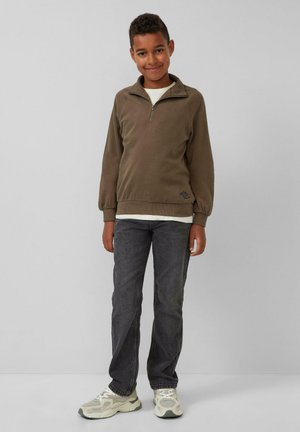 Bruine sweatshirt met rits en lange mouwen, gecombineerd met donkere jeans en lichtgekleurde sneakers. Heeft een logo-detail aan de voorkant.
