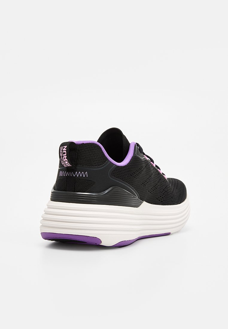 Zapatilla deportiva negra con acentos morados, parte superior de punto texturizado, media suela acolchada y suela exterior blanca en contraste. Presenta cierre de cordones y detalle del logo.