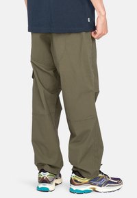 Olijfgroene cargobroek met een relaxte pasvorm, uitgerust met meerdere zakken en een lichte, gestructureerde stof, gecombineerd met meerkleurige sportschoenen.