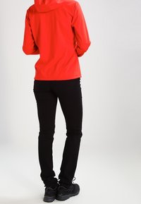 Chaqueta con capucha roja, pantalones ajustados negros y calzado negro. La tela parece suave y ligera, ideal para ropa de exterior.